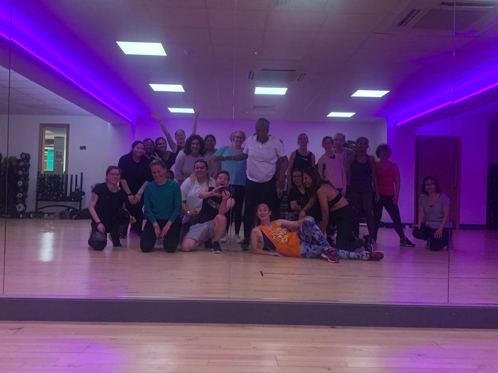A large class posing in front of the studio mirror under purple lights